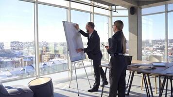 Cheerful businessman and a secretary work in office. Office workers developing new strategy together indoors on windows background of the city. video