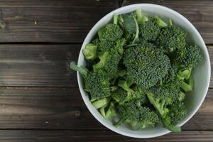 Fresh green broccoli in bowl on wooden background, table top view, empty space photo