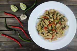 Oseng tempe or stir fry tempe with chili on white plate, against plank wooden background, with red chilli photo