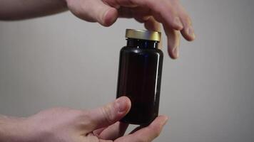 Close-up of hands opening a jar with different pills and pouring handful into palm of their hand on abstract white background. video