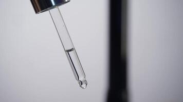 Close-up of a pipette containing a clear liquid, positioned against a simple white background, with drops steadily dripping from it. Studio shot video