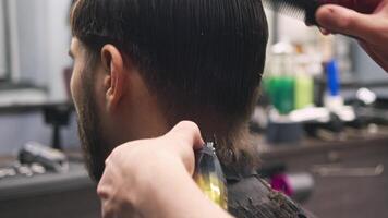 Hairdresser creates a clear outline for the haircut on the back of the client's head, using a clipping and shaving machine and a comb. video