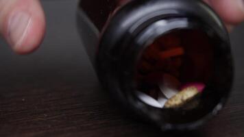 Diseased inadvertently knocked over jar of various pills on table, causing several pills to fall out of it. Then patient collected pills. Close up. video