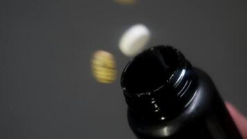 Pile of pills are poured out one after another from top of bottle, directly at camera, in blurred image. POV. Slow motion. Close up. Studio shot. video