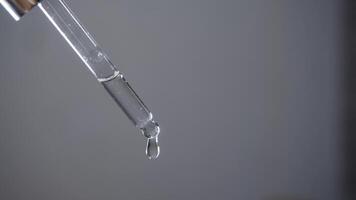 Detailed view of pipette filled with a transparent liquid, set against a plain white backdrop, with drops falling from it in a steady stream. Studio shot. video