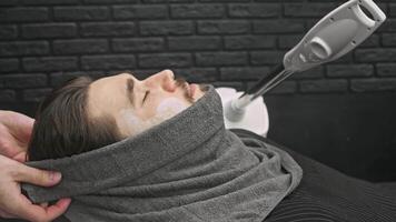 Man's face, with shaving cream applied to his cheeks, is wrapped in hot, moist towel and steamed using steamer to soften skin for shaving. video