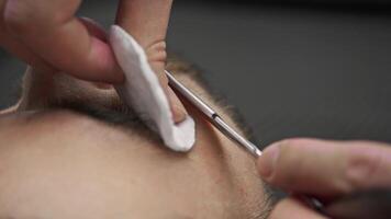 Using straight razor with sharp blade, barber carefully removes the stubble from client's cheek, then wipes it with cotton pad and soothing lotion. video
