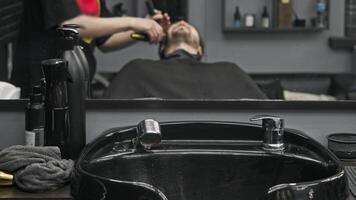 A black ceramic sink is used for shampooing at the barbershop, and the process of shaving a beard is visible in the mirror. video