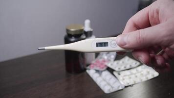 A large assortment of medicines and containers is laid out on the table, and in the foreground is a thermometer showing a typical temperature for a recovered person, which is 36 degrees Celsius. video
