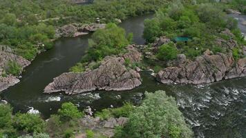 Aerial view of a rough river among the rocks. Mountain river running through a rocky canyon. Trees and large stone boulders around. Gusts of wind swaying tree branches. video