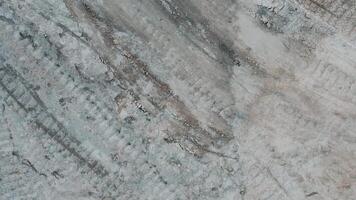 Aerial view of a gray and white dry ground texture with cracks. View from a drone taking off on a dry, cracked soil surface with traces of tracked vehicles. video
