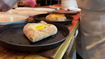 Chef adds raw egg yolk and butter to baked Adjara khachapuri with suluguni cheese at restaurant. video
