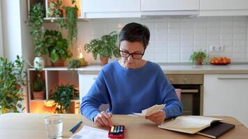Unhappy exhausted mature woman calculating household expenses on smartphone at home. Reviewing bill video