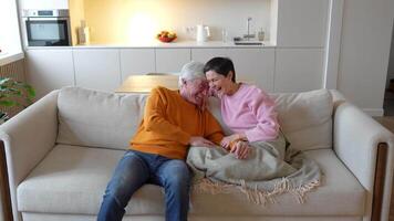 Senior couple laughs have fun relax on sofa at home. Smiling joking fooling around enjoying together video