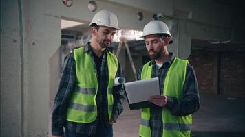 Two glad Caucasian men builders discuss building project in construction architects handymen talking paper draft workmen guys working document manufactory contractors smile shake hands deal handshake video