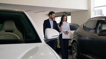 kaukasisch Mann Klient wählen zwischen zwei Autos kommunizieren mit Frau Händler Händler Berater Portion Beratung Leasing Handel Neu Auto gehen im Automobil Salon Ausstellungsraum wählen Auto Miete Bedienung video