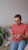Vertical , Man at home on bed using smartphone, taking off glasses and rubbing eyes from tiredness and discomfort in eyes. Vision problems video