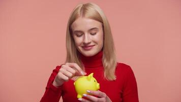 Smiling woman saving money in piggy bank on pink background video