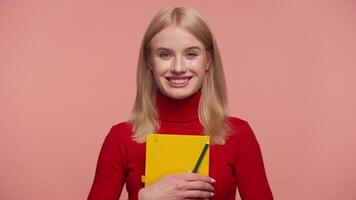 Smiling student holding notebook and pencil on pink background video