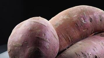 Raw sweet potatoes in a mountain gyrating on black background. Ipomoea Batatas video