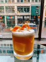 Craft cocktail with citrus garnish on a table near a rainy window in an urban environment photo