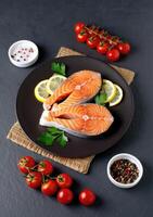 Fresh salmon fillets garnished with herbs and accompanied by ripe tomatoes and lemon slices photo