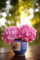 Beautiful pink hydrangeas in a decorative vase on a wooden table during golden hour photo
