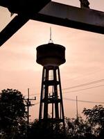 Silhouetted Water Tower Against a Warm Sunset Sky with Trees and Power Lines in the Foreground photo
