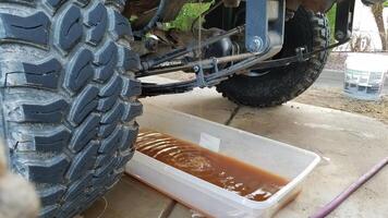 Draining the Antifreeze on a 1990s Vehicle with Big Tires into a Plastic Bin photo