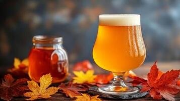 Sweet maple flavored craft beer in snifter glass with caramel glow, maple syrup jar and autumn leaves photo