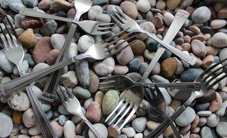 Heap Of Cake Forks And Table Forks On A Colored Sea Stones Closeup View photo