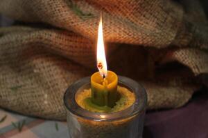 Natural Wax Candle Burns In Glass Cup With Wheat Grain On Burlap Background photo