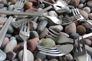 Same table forks and cake forks from the cutlery set scattered on colored pebbles photo