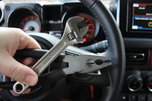 Mechanic holds repairing tools in front of the steering wheel and blurred instrument cluster in car photo