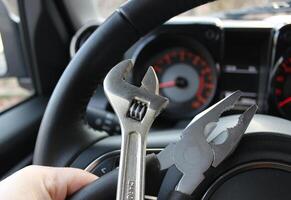 The driver holds in his hand set of tools for repair in front of the blurred car tachometer in vehicle with the ignition on photo