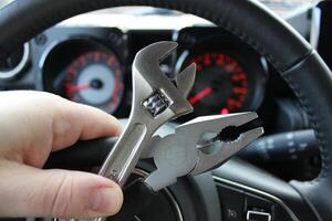 Pliers And Adjustable Wrench In Human Fingers In Front Of Defocused Car Dashboard With Red Digits And Arrows photo