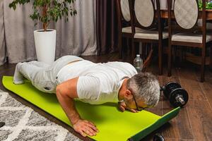Man exercising with push-ups on a green yoga mat indoors photo