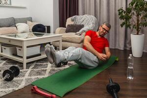 Man exercises at home on mat with dumbbells nearby photo