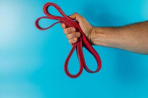 Hand grips a red resistance band against a blue background photo