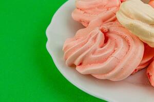 Freshly made meringues on a white plate with green background photo