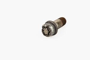 Broken bolt lying on a surface with a damaged wheel nearby photo