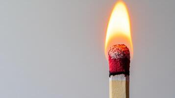 Close up of burning matchstick with bright flame and charred tip against plain light background, showing intense heat and energy photo