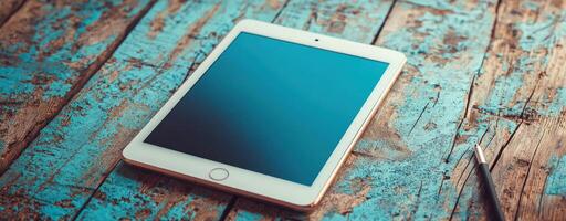 Tablet on rustic wooden table with blue paint and stylus nearby, clean product shot with natural tones and ample empty space for text photo