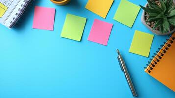 Colorful sticky notes arranged on blue desk with notebook, pen, and small plant creating organized and vibrant workspace scene photo