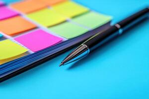 Open planner with colorful sticky notes and sleek black pen resting on bright blue surface, creating organized and vibrant workspace photo