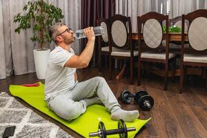 Man resting after workout and drinking water at home photo