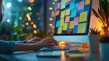 Close up of hands typing on keyboard with colorful sticky notes on computer screen in cozy workspace with warm lighting and plants photo