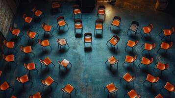 Dramatic overhead shot of multiple orange chairs arranged in synchronized circular layout on concrete floor, creating striking pattern photo