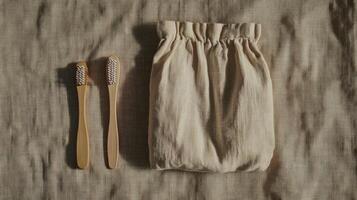 Flat lay of two bamboo toothbrushes and a linen pouch on a textured beige surface. Sustainable and natural dental care items photo