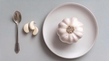 A white plate with a garlic bulb and spoon photo